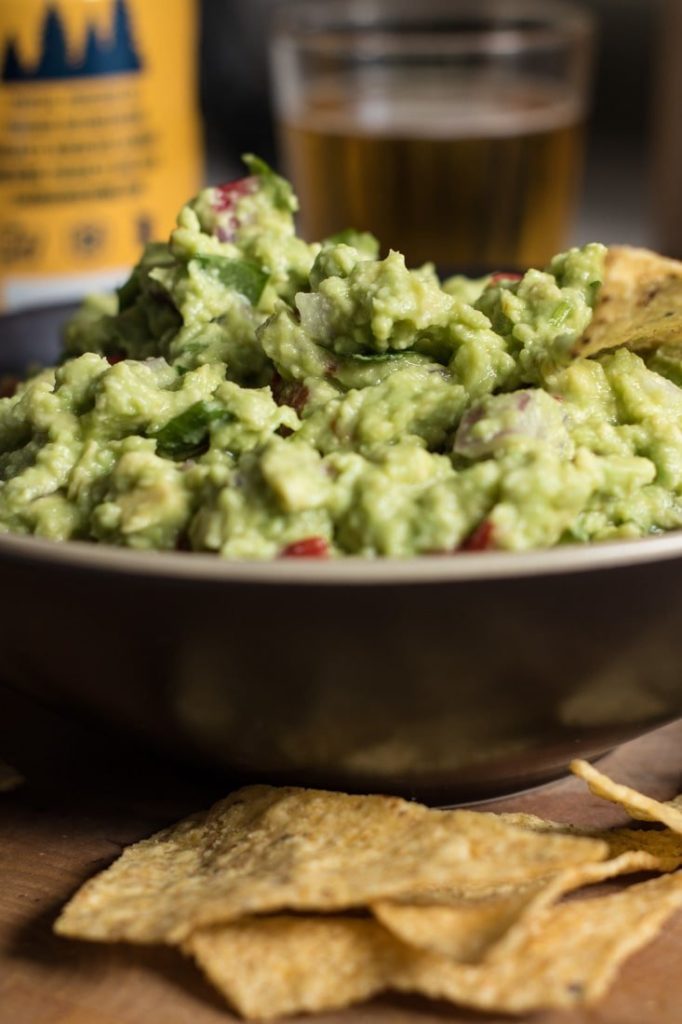 How to make an amazing easy guacamole, on a bowl above wooden board, with tortillas around the bowl