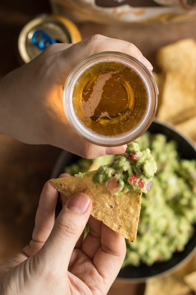 Close up of hands holding beer and tortilla with guacamole