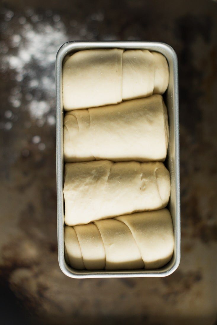 Japanese milk bread dough in a loaf pan over a rusty tray.