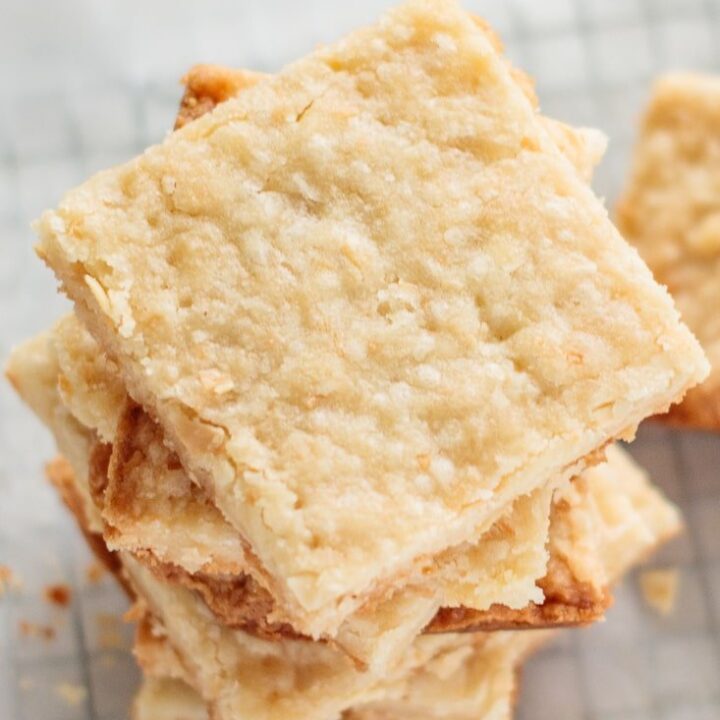 almond coconut shortbread bars, stocked one above another, on parchment paper, with crumbs all over it.
