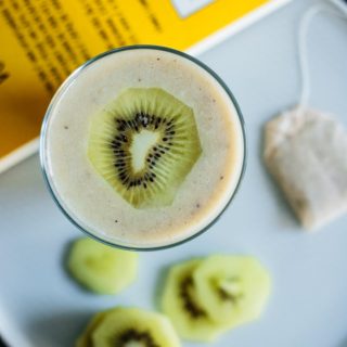 flat lay of glass full of good night smoothie with kiwi slices and a chamomile tea bag over a blue plate