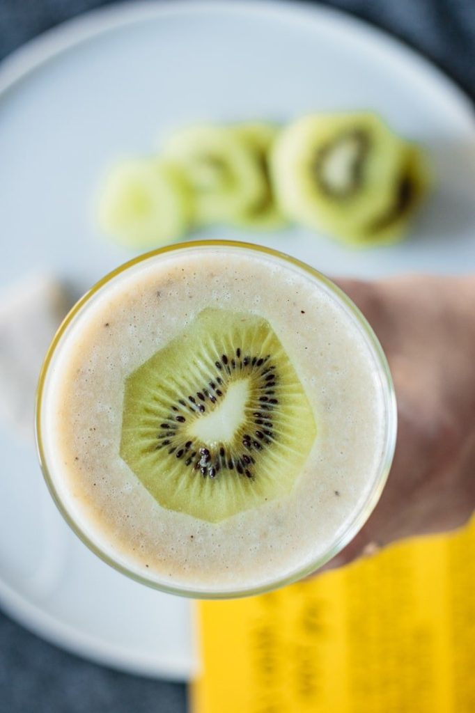 glass full of recipe with kiwi slices and a chamomile tea bag over a blue plate and yellow book cover