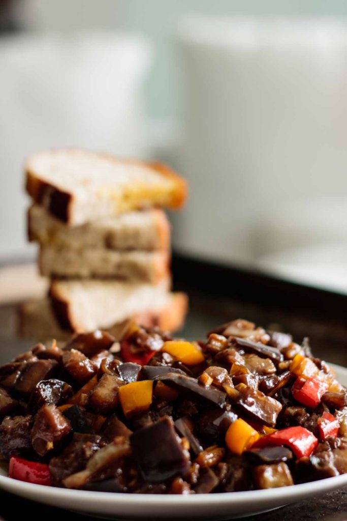 a plate full of caponata with a stack of bread on the background