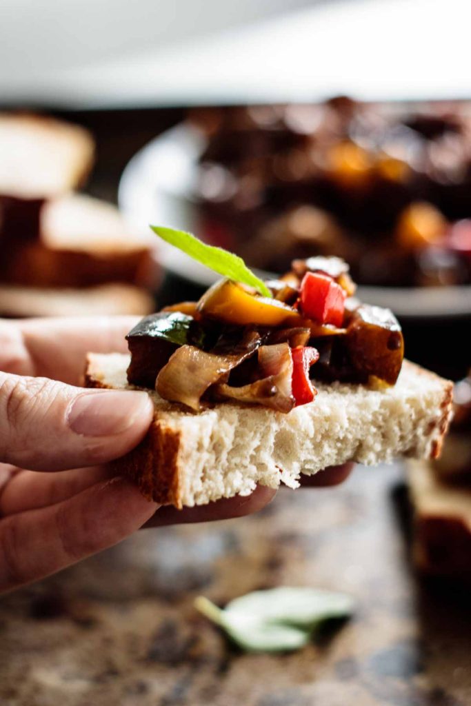 caponata over a sourdough toast held with caponata on the background