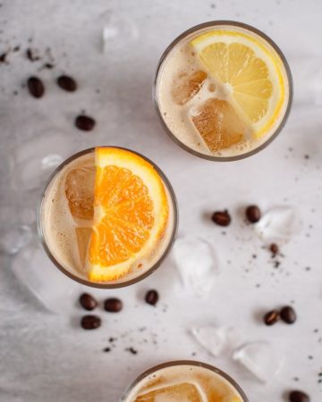 three glasses of coffee lemonade decorated with lemons and orange slices, filled with ice, coffee beans and ice on the background,