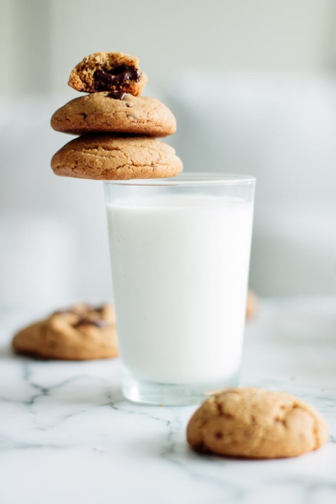 a glass full of milk and a stack of 3 peanut butter chocolate chunk cookies, with one half eaten