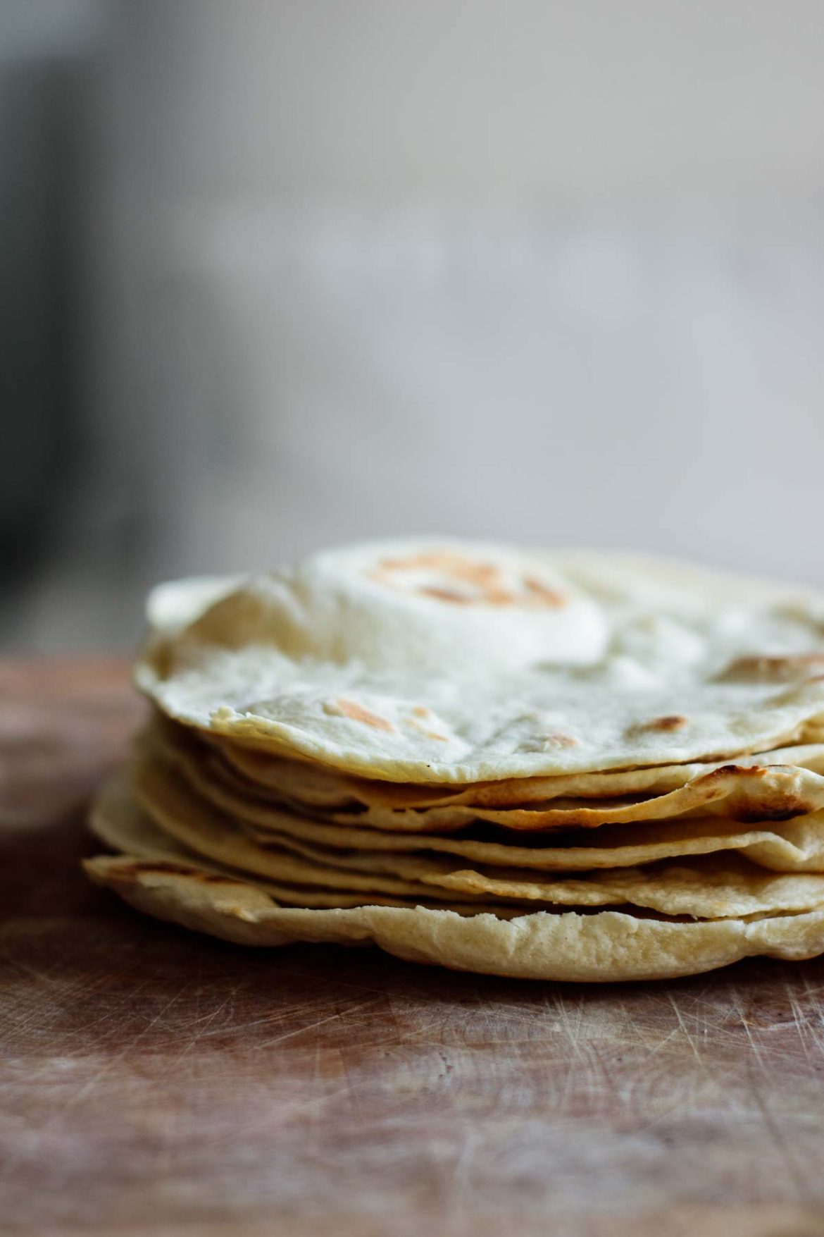 Fried sourdough tortillas stacked over wooden board.