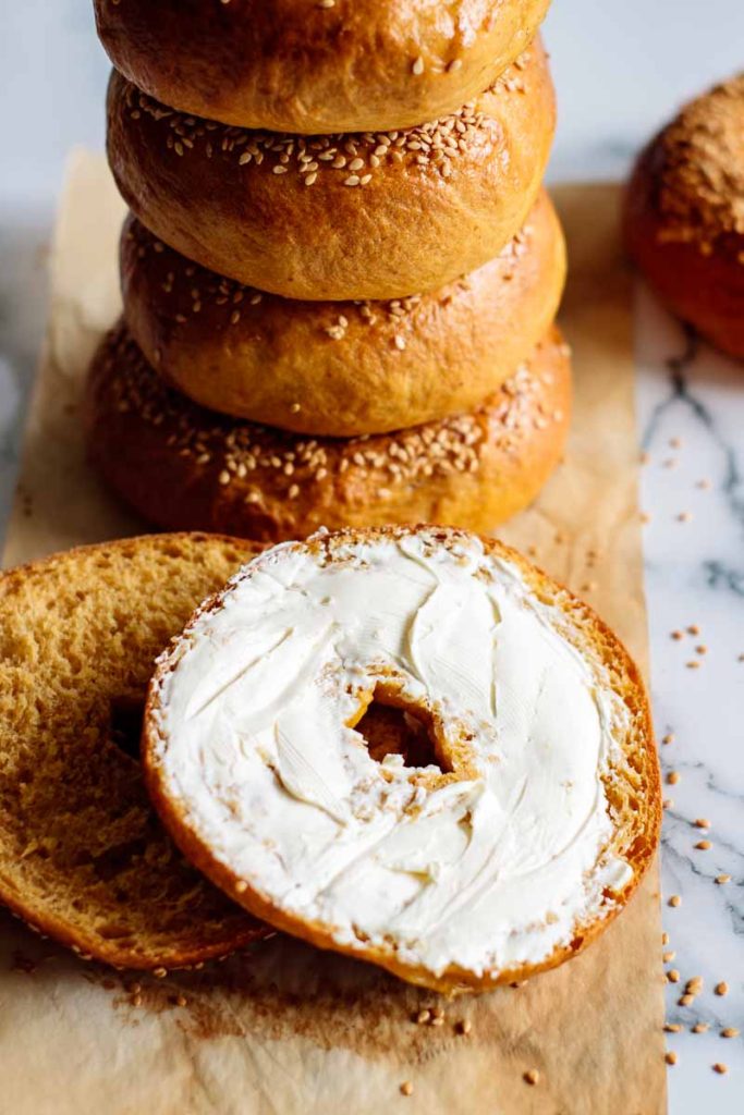 pumpkin bagels, one stack of bagels, one sliced in half with cream cheese spread