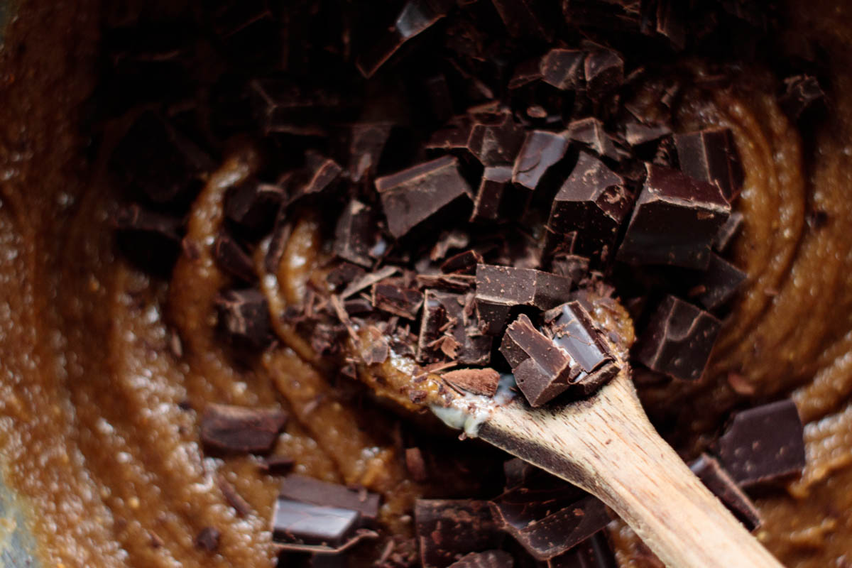 chopped chocolate being add on cookie dough, with wooden spoon mixing everything