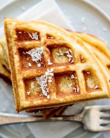 A stack of coconut flour waffles, with coconut flakes on the top.