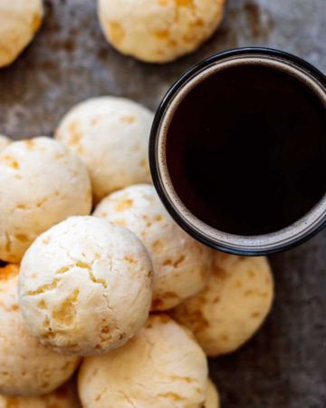 a stack of cheese bread with a cup of black coffee