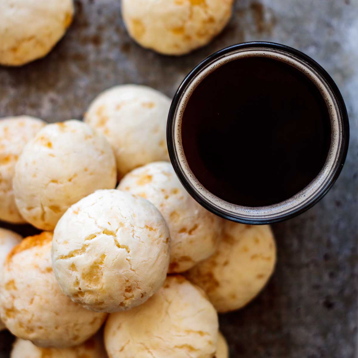 a stack of cheese bread with a cup of black coffee