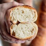 french baguette cut in half, showing its interior, soft and chewy, with baguettes in the background