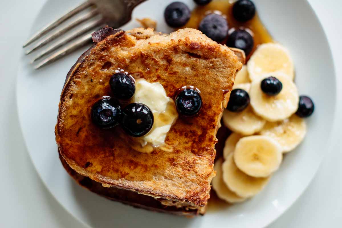 sourdough french toast with butter, berries, banana and maple syrup seen from above