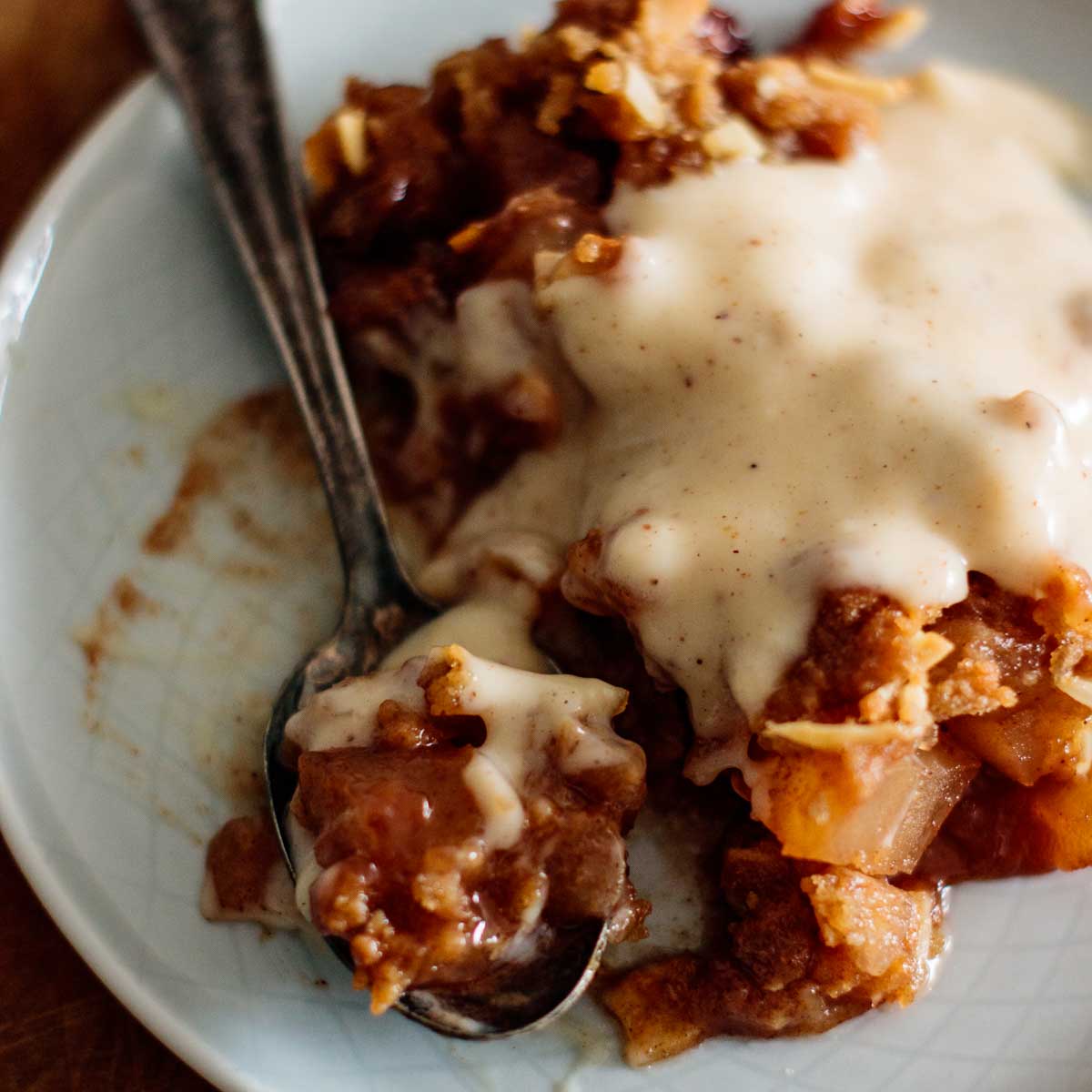 Apple crisp with eggnog sauce in a plate with spoon.