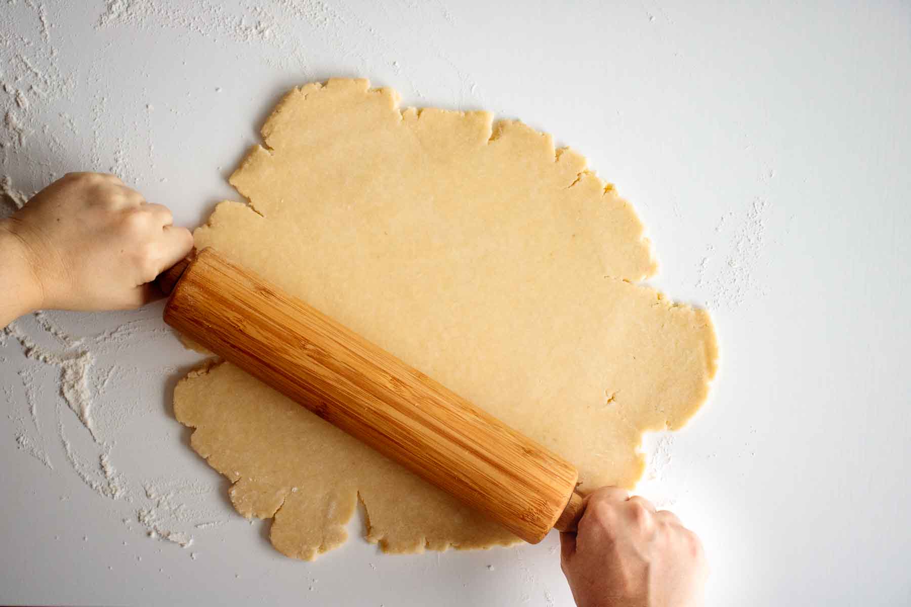 Pie crust dough being opened with a rolling pin.