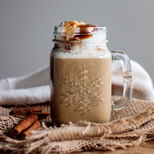 cinnamon dolce latte on a wood table, served in a glass mug, with cinnamon spice resting beside it.