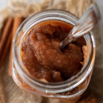 A jar of apple butter with spoon inside.