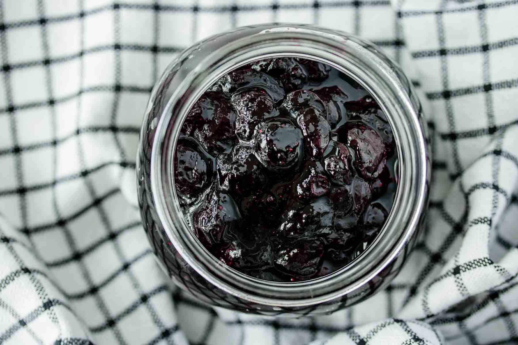 a jar of blueberry compote over a kitchen towel