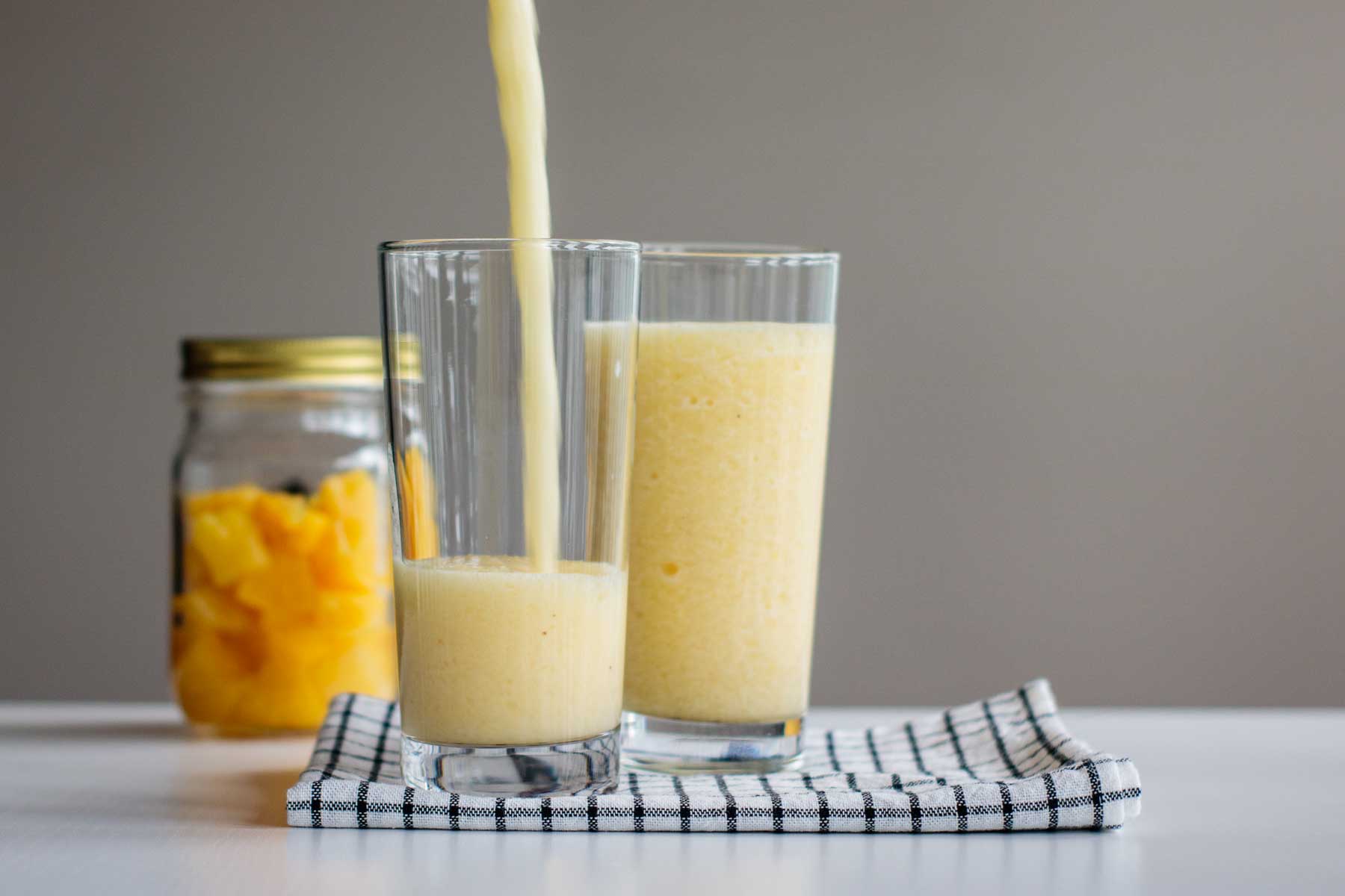 hangover smoothie being poured in a glass cup, with pineapple chunks in a jar on the back