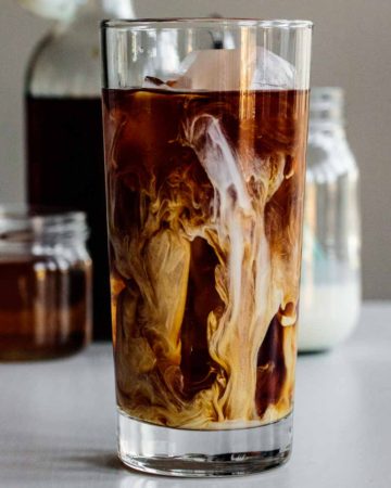 a tall glass of vanilla sweet cream cold brew with cream, syrup and coffee in the back