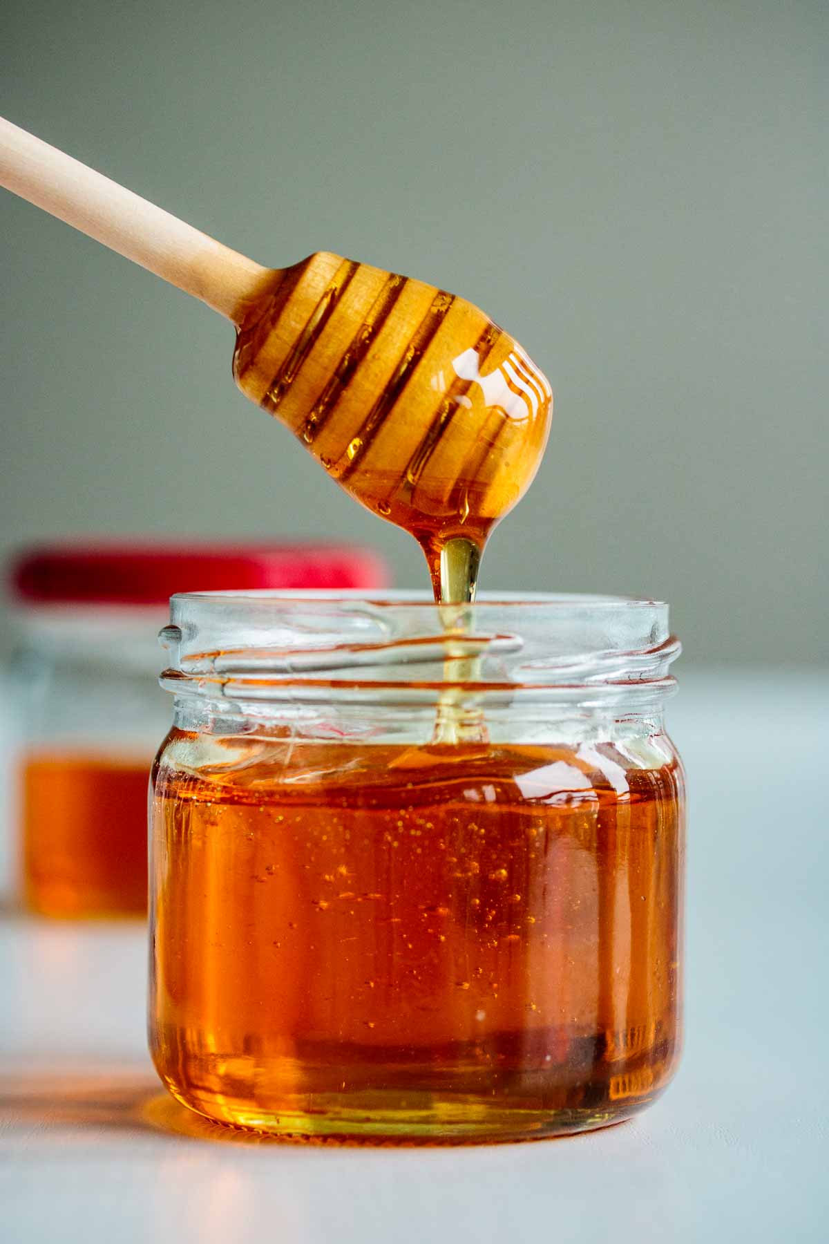 a jar filled with vegan honey, showing its consistency dripping off a honey dripper