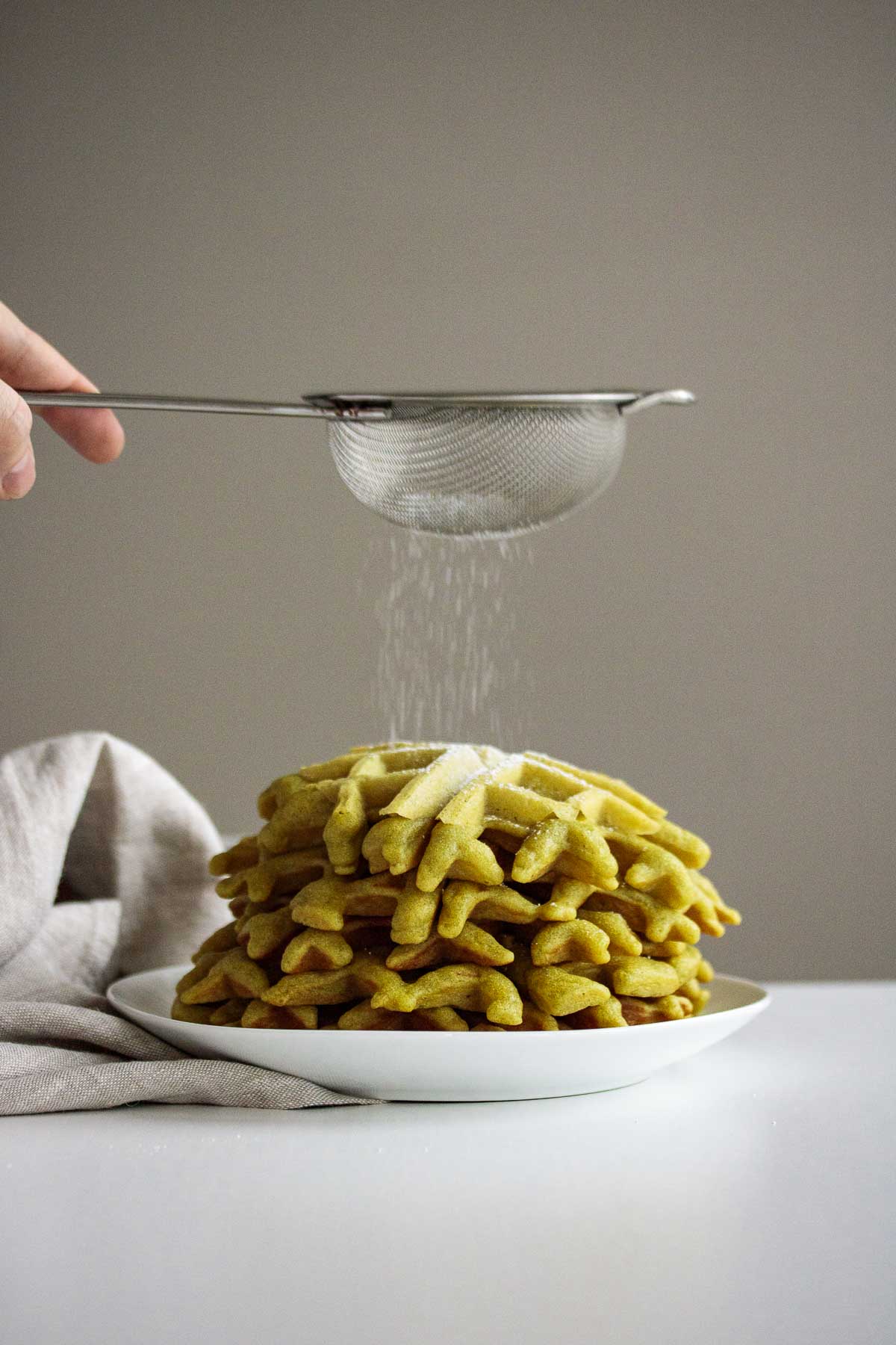 A stack of green waffles with sugar sprinkled on top.