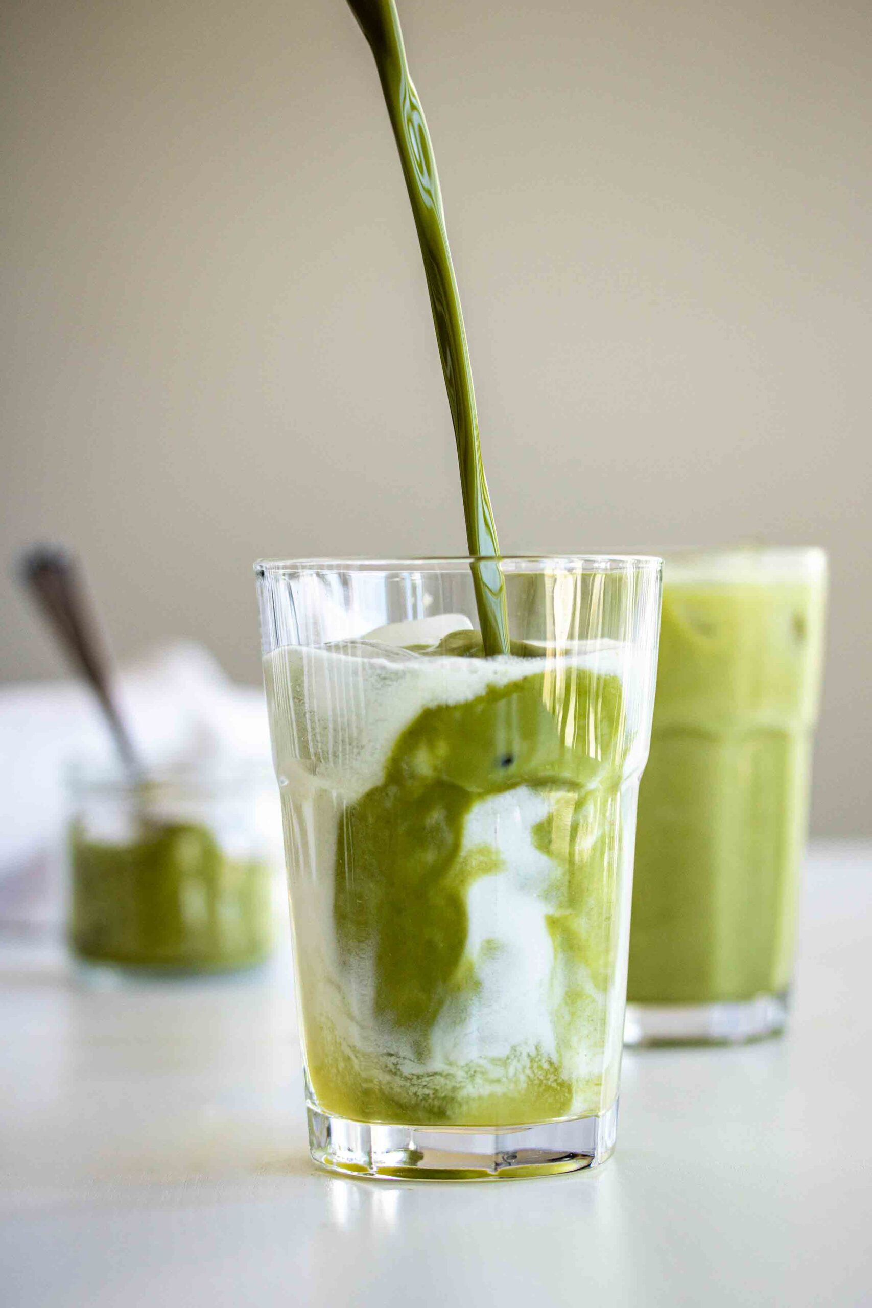 Matcha being poured in a glass with ice cubes, coconut milk and pineapple ginger syrup.
