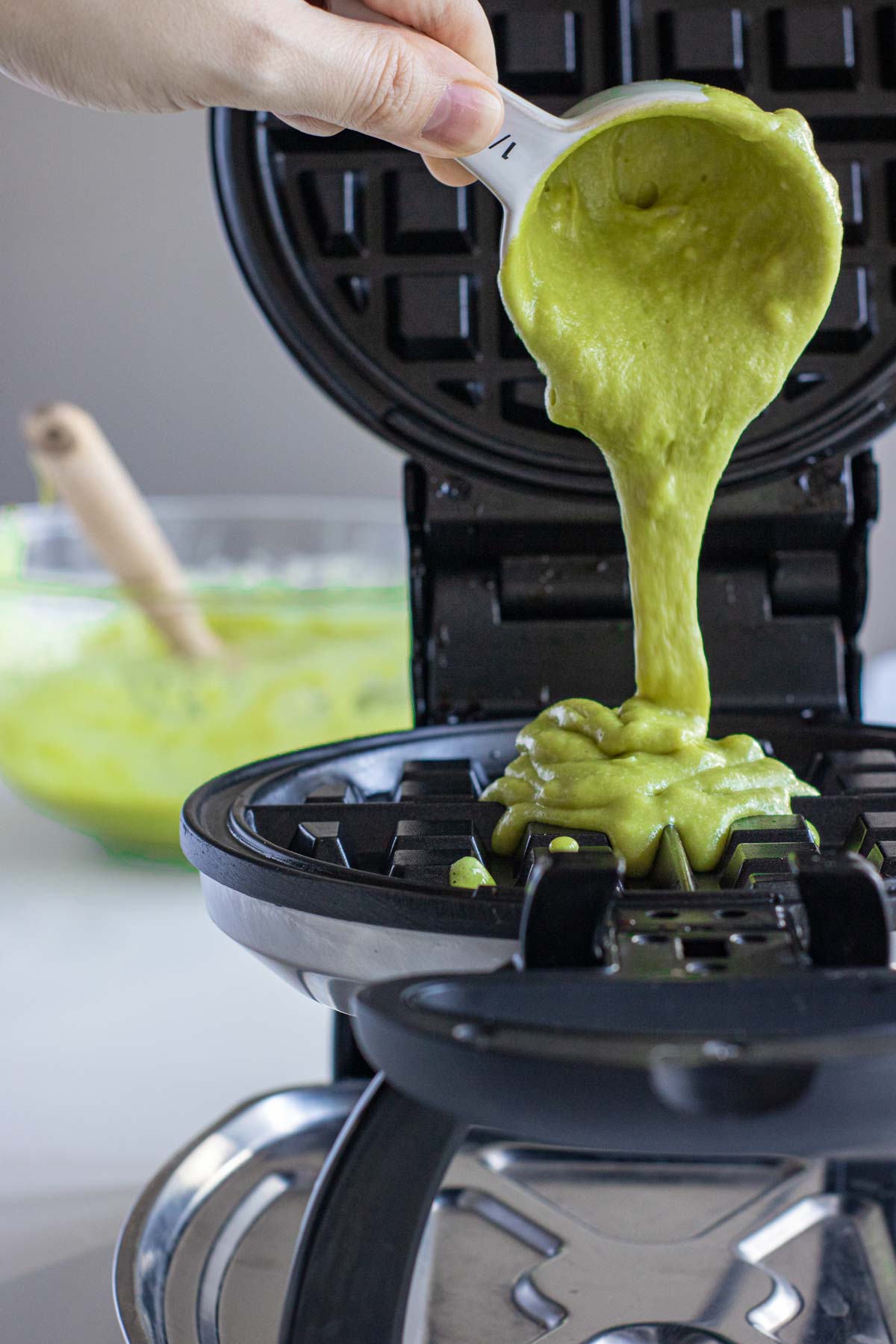 Pouring green batter in preheated waffle maker.