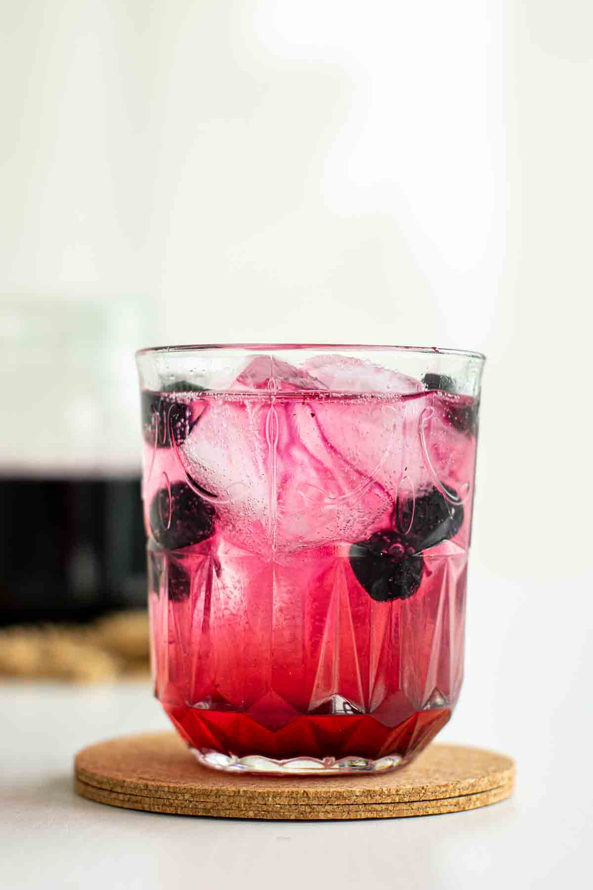 A glass og homemade blueberry soda with blueberries and ice.