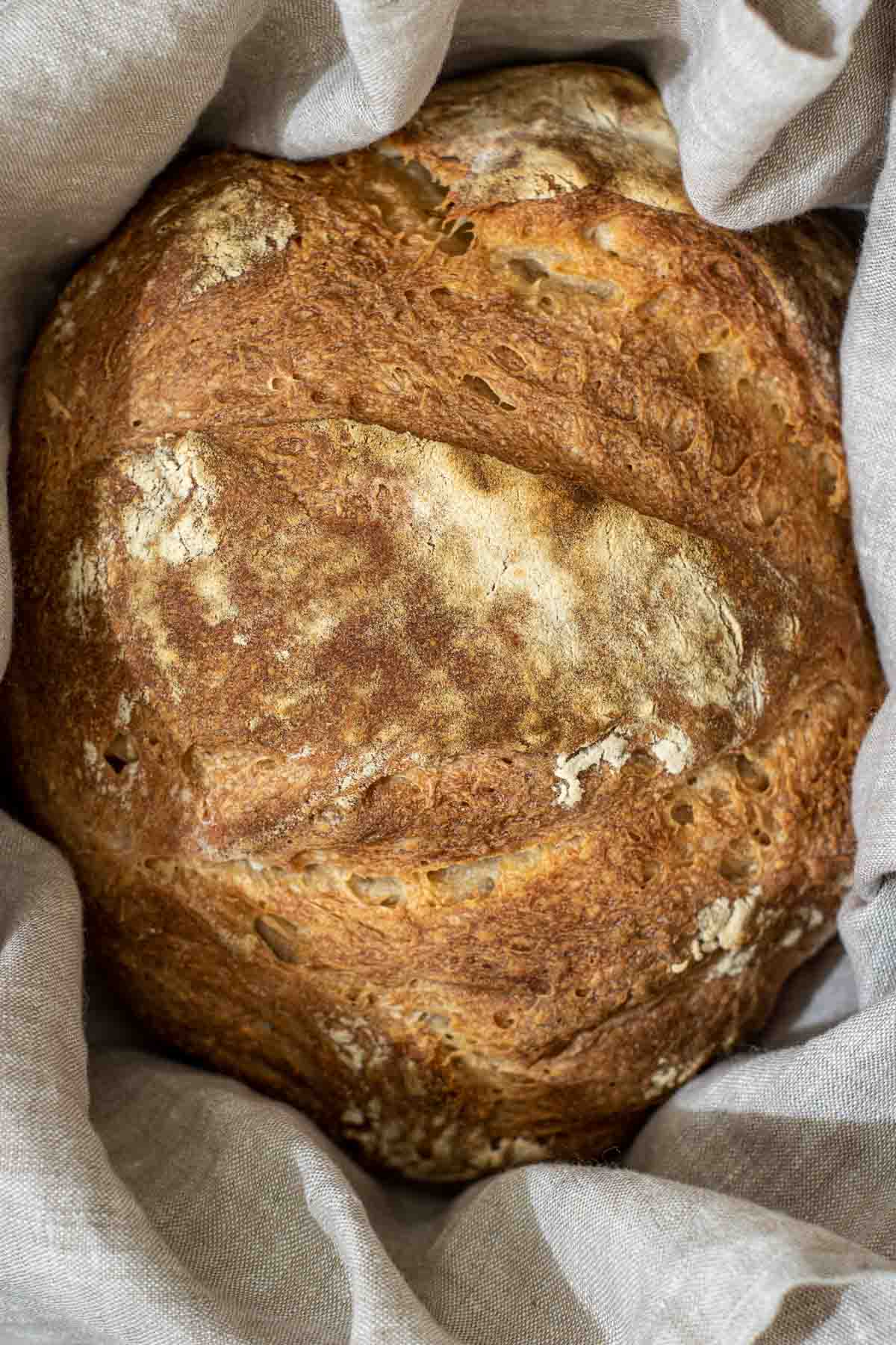 close up of bread crust stored in a dutch oven over linen towel