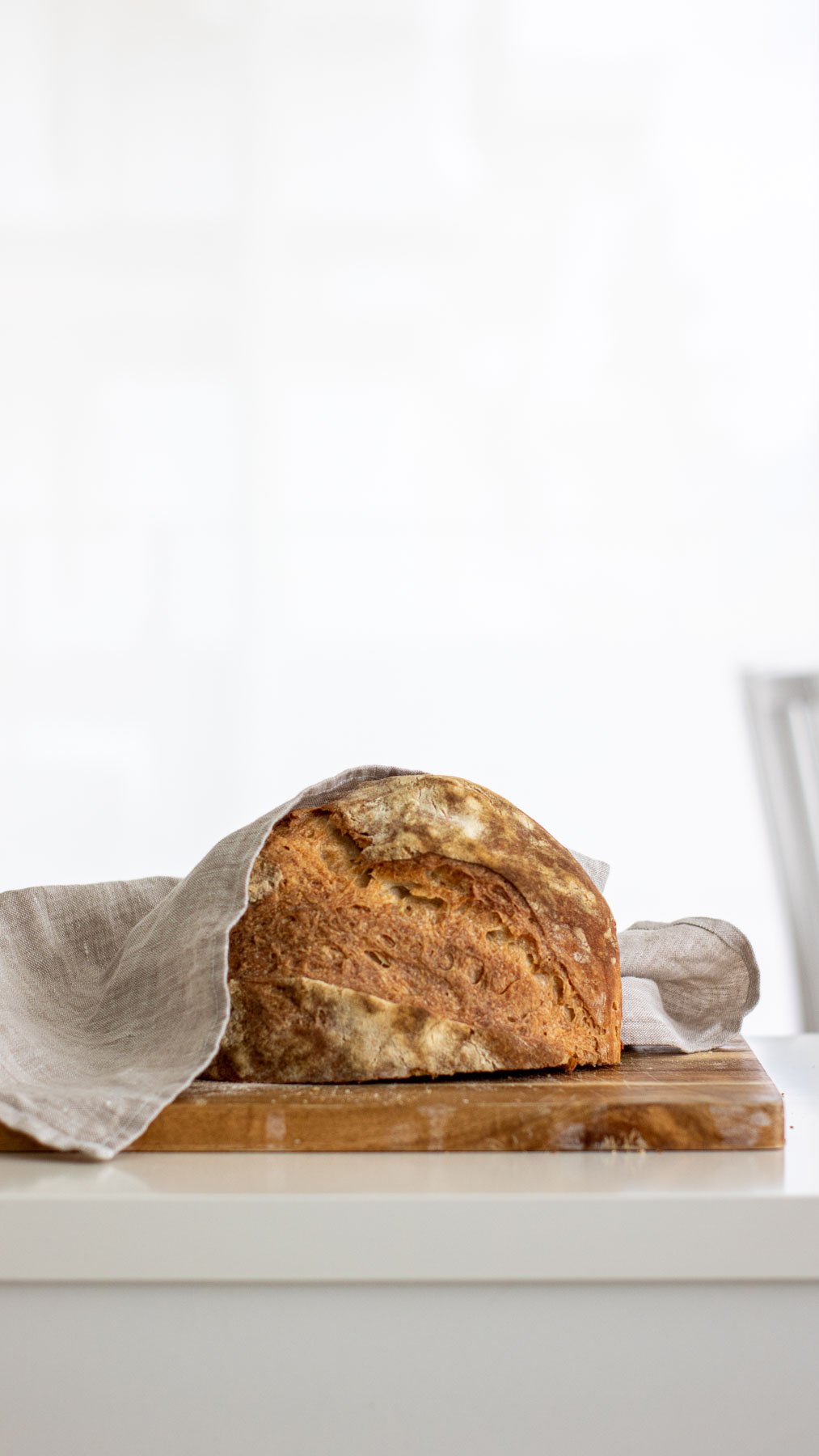 Bread stored with the cut side facing lanugo over a wooden board, with linen towel dropped over it.