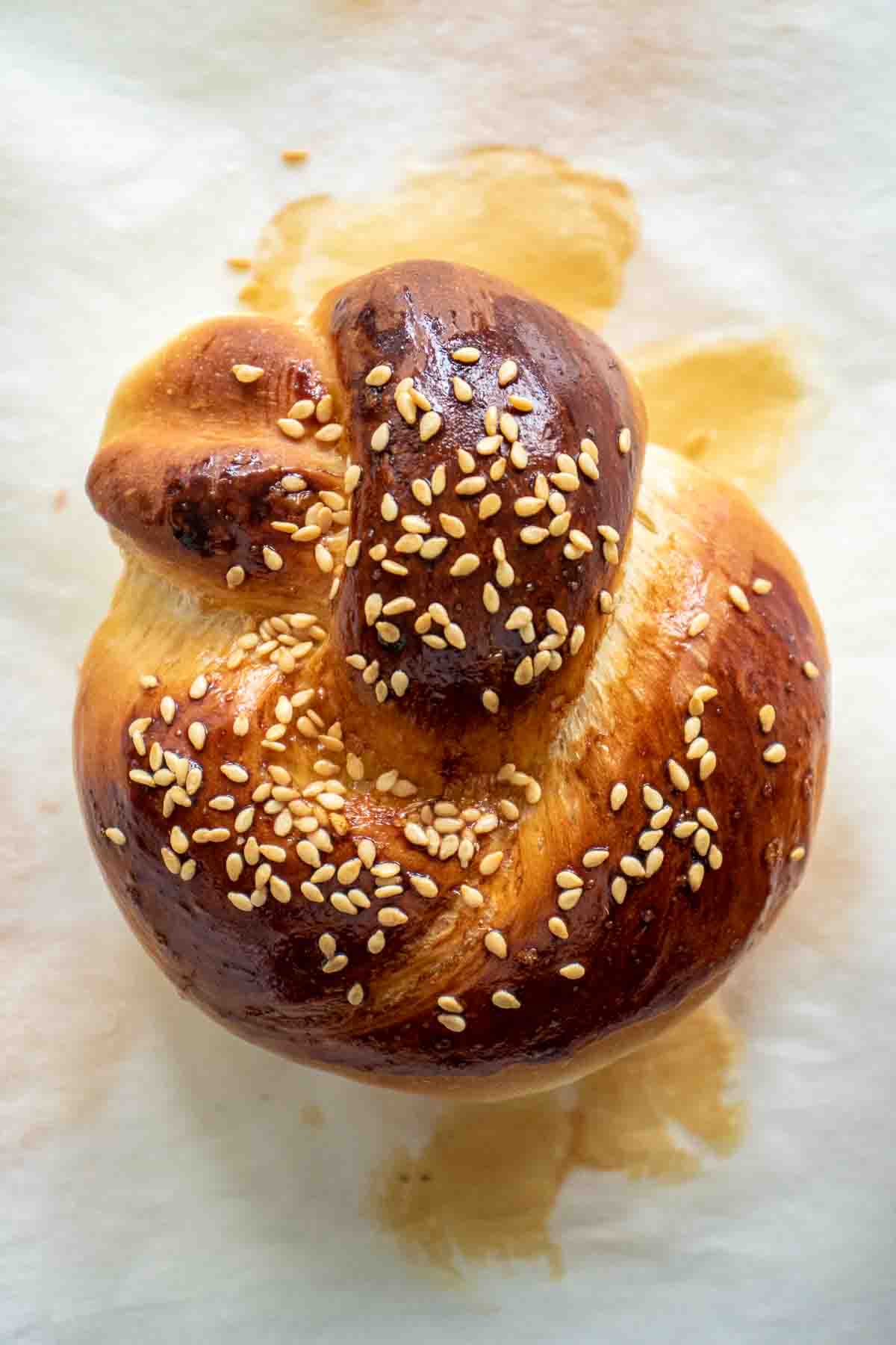 A baked challah roll over parchment paper.