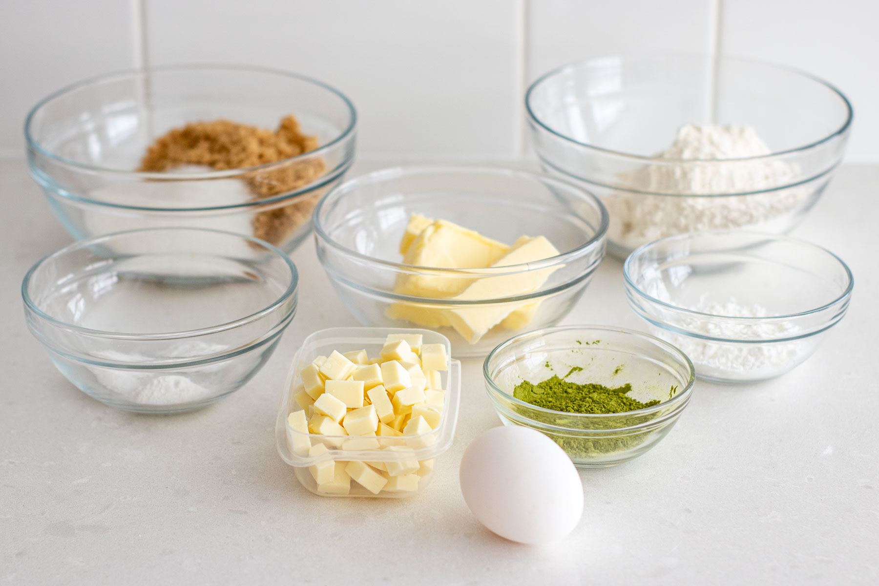 Ingredients of the matcha cookies recipe, separated in clear bowls.