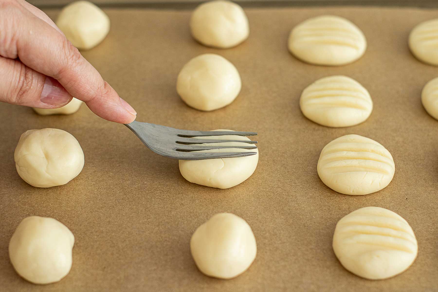 Fork flattening cookies in a baking sheet lined with parchment paper.