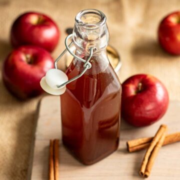 A bottle of apple brown sugar syrup, with apples and cinnamon sticks.