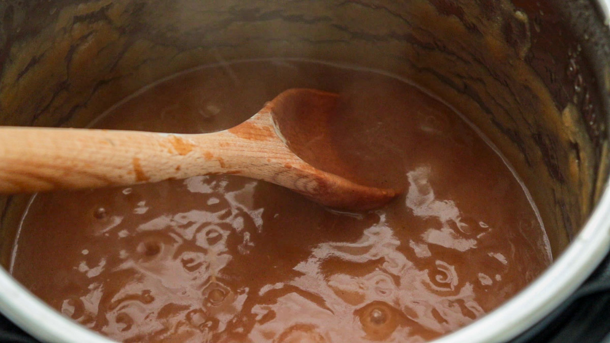 Apple butter cooking on a pressure cooker with a wooden spoon inside.