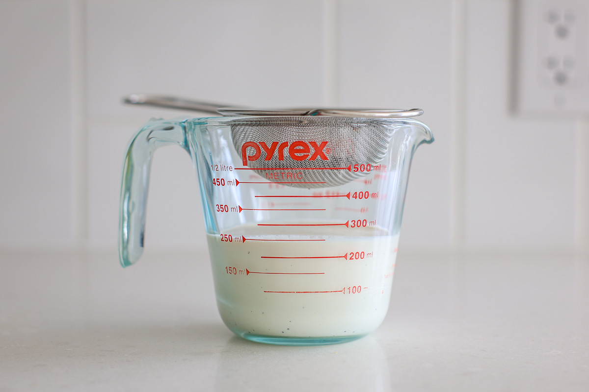 Strained heavy cream inside transparent glass container, fine mesh strainer with loose Earl Grey tea.