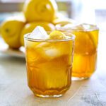 Brown sugar lemonade over ice in two glasses with lemon slices and lemons on the background.