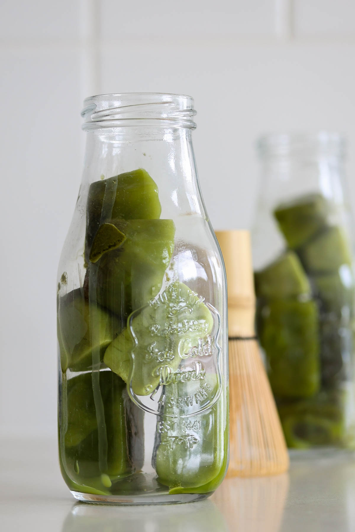 Two bottler full of matcha ice cubes, and a bamboo whisk.