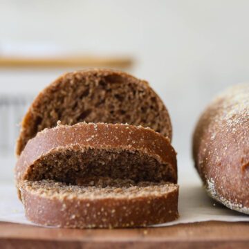 Sourdough molasses brown bread rolls sliced over a wooden board.