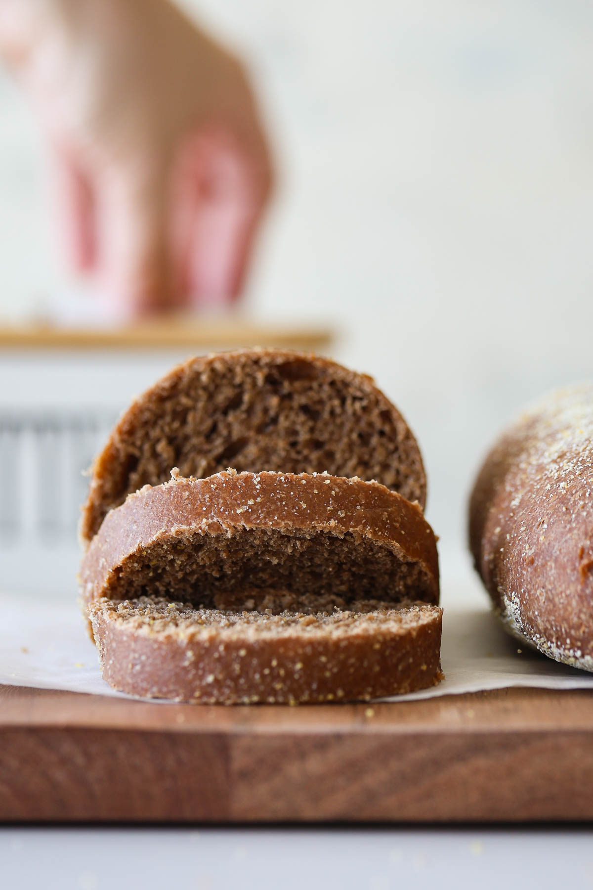 Sourdough brown bread roll, sliced, on a wooden board and parchment paper.