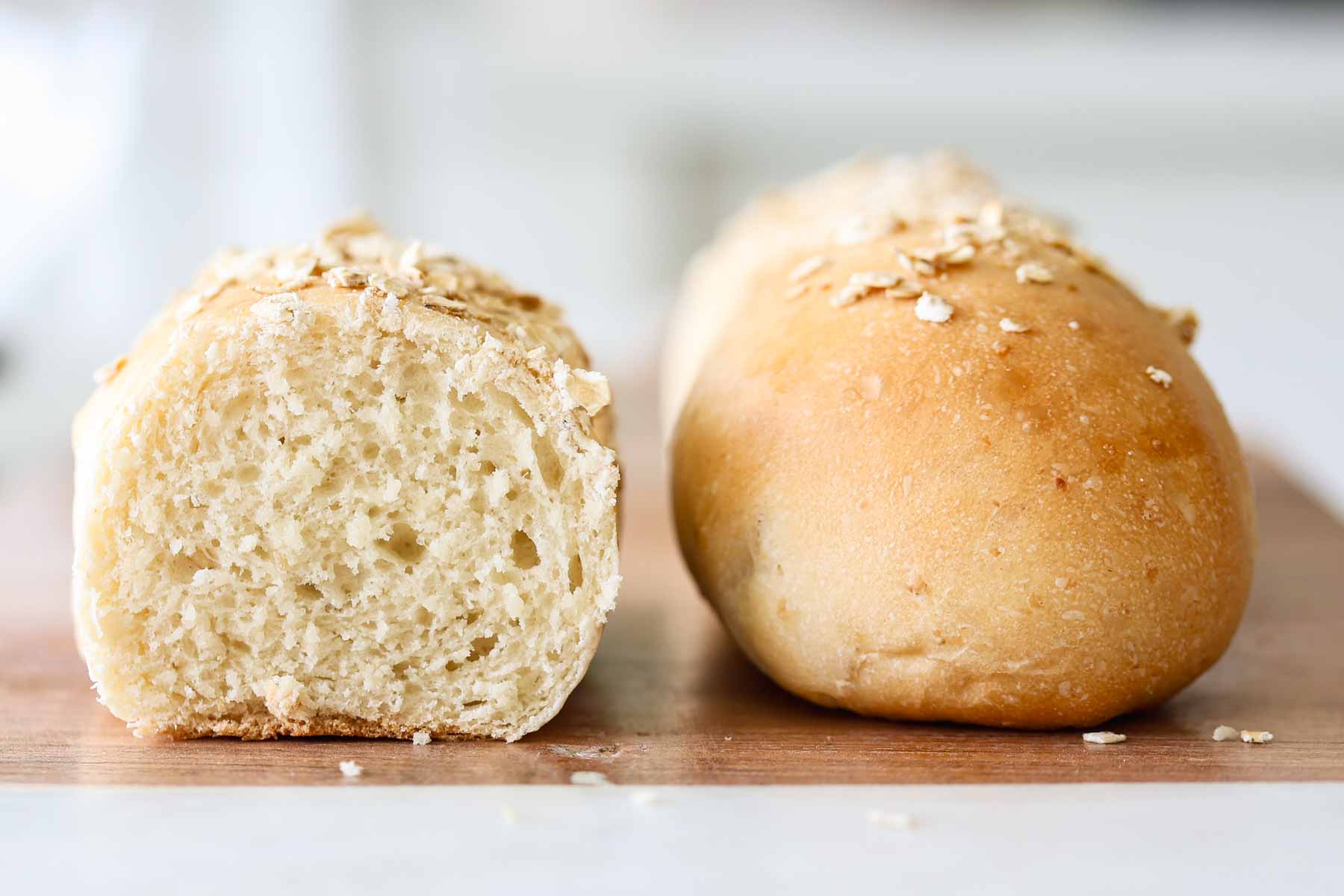 Two rolls, one sliced, showing its soft crumb, the other one whole, on a wooden board.