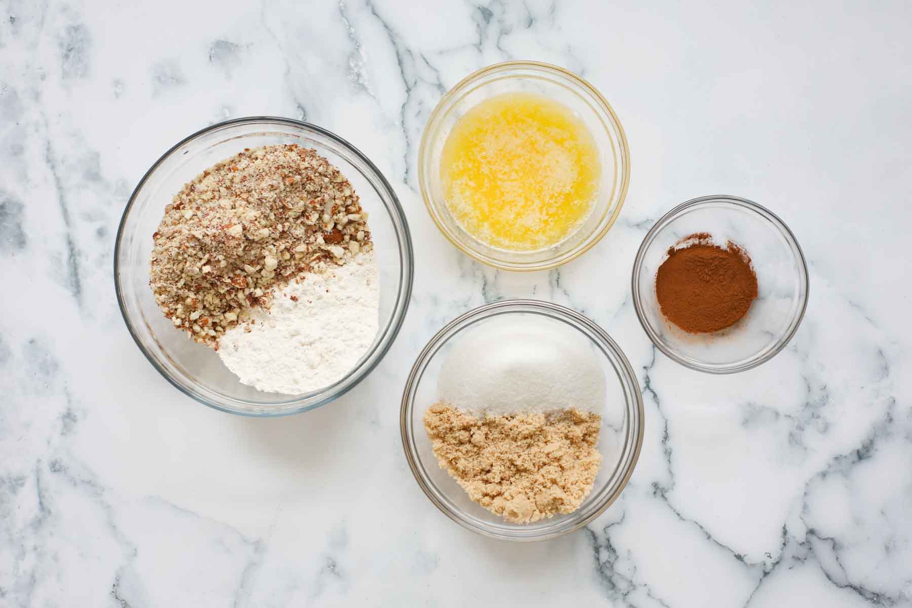 Glass bowls with chopped almonds, flour, sugar and brown sugar, cinnamon and melted butter.