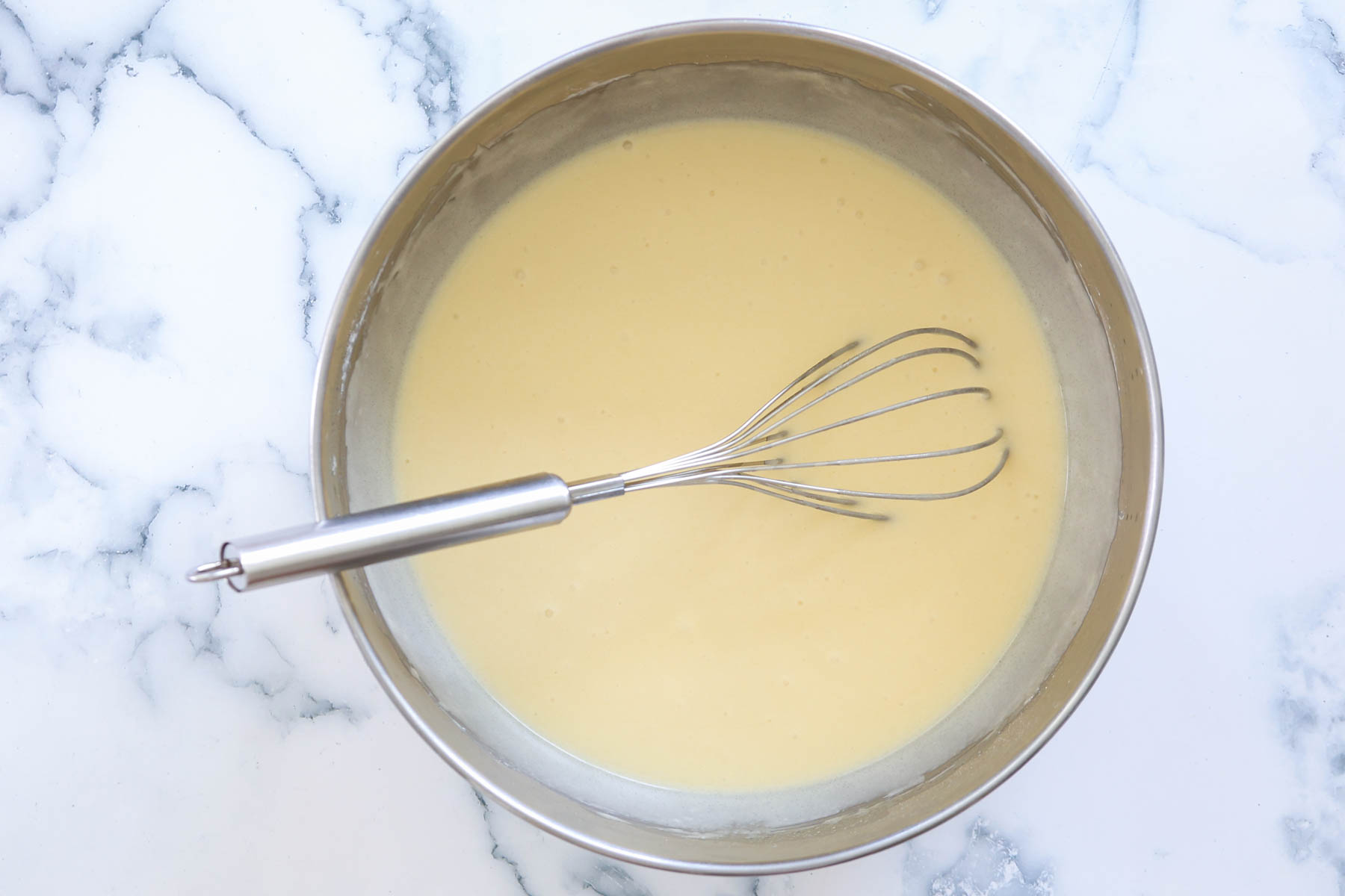 Cake batter with whisk inside metal bowl.