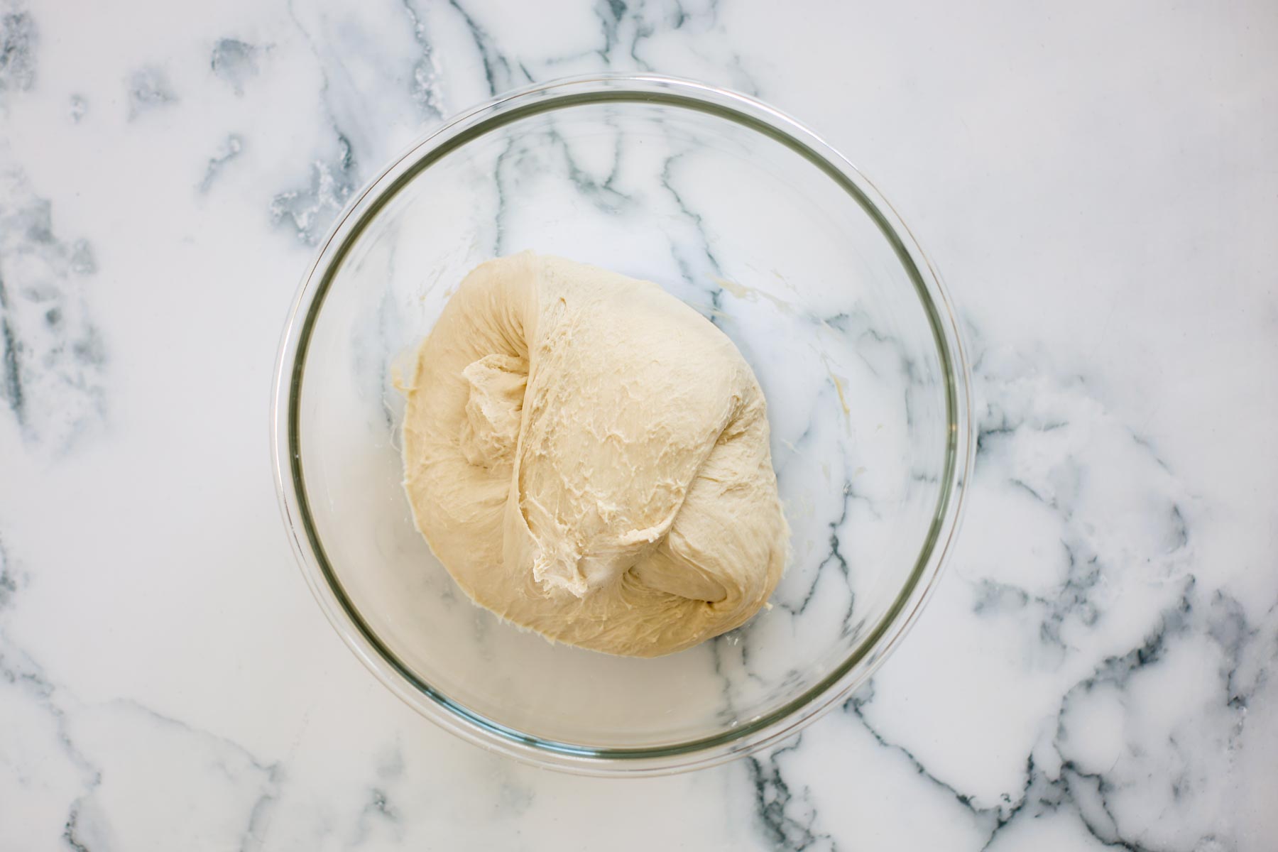 Dough folded over itself in a glass bowl.