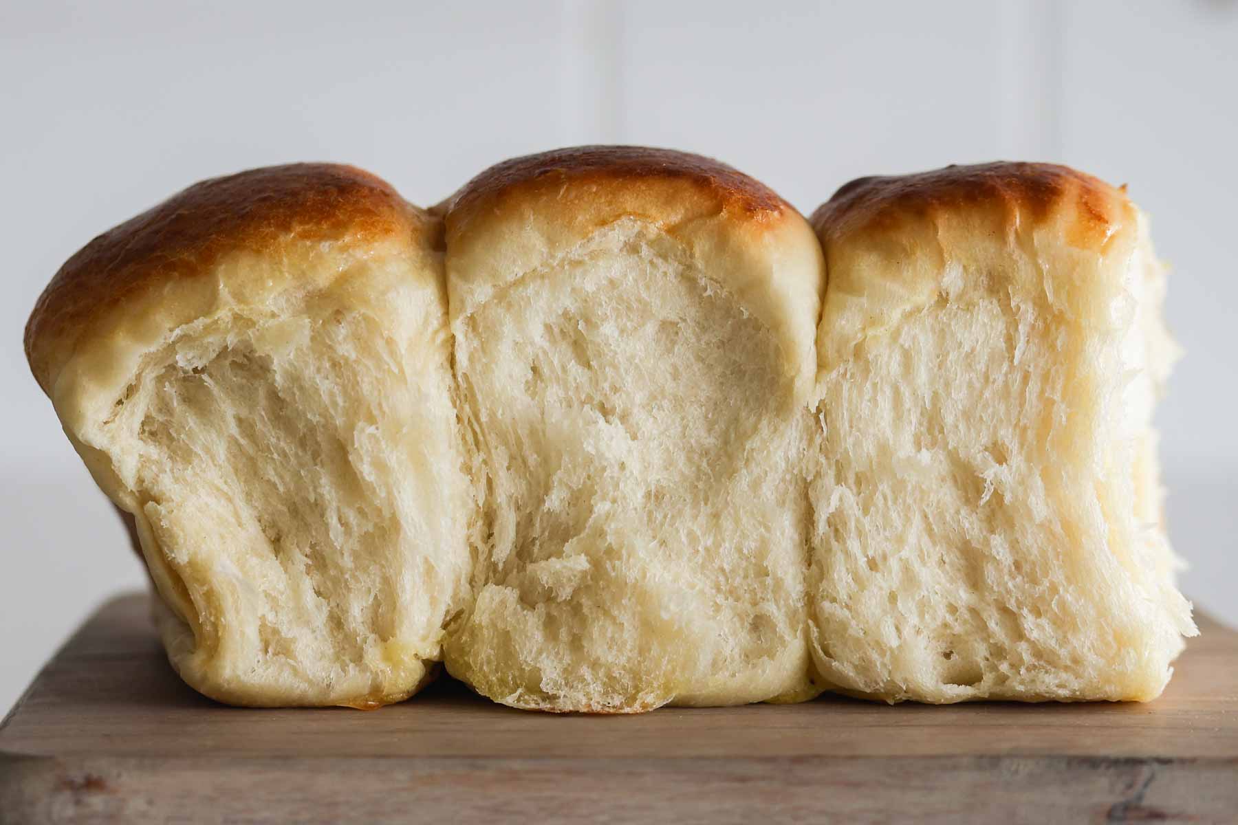 Three Hawaiian rolls on top of a wooden board.