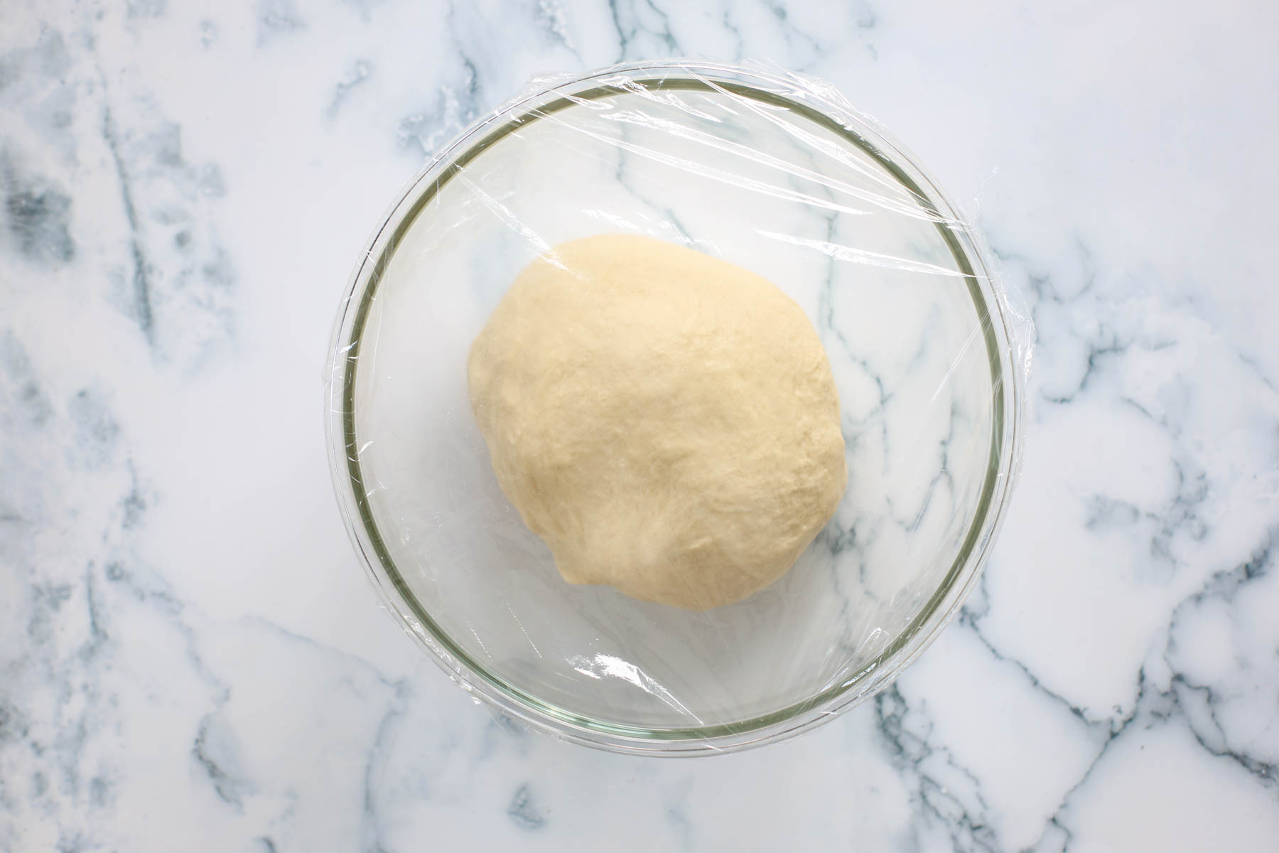 Dough covered with plastic wrap inside glass bowl.