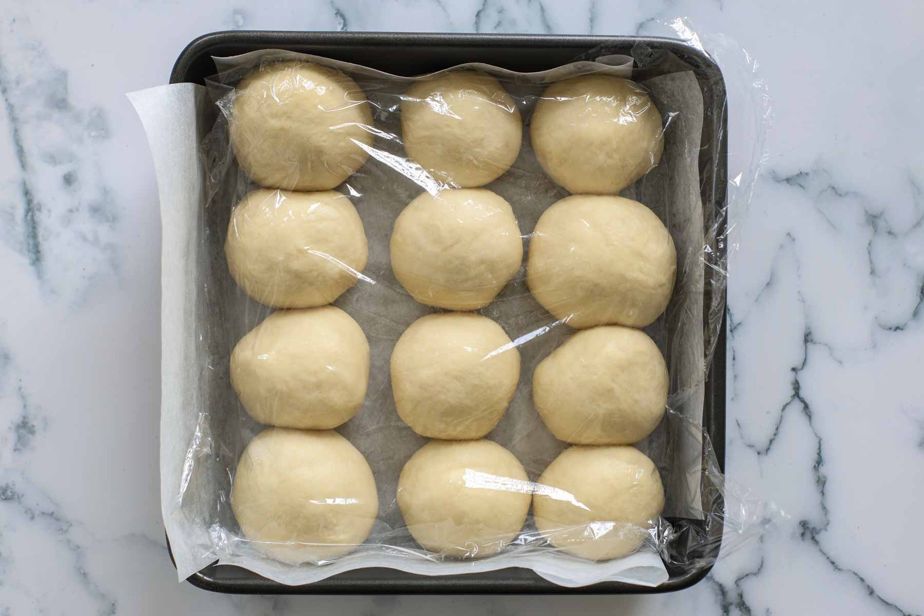 Rolls proofing inside a baking sheet with parchment paper.