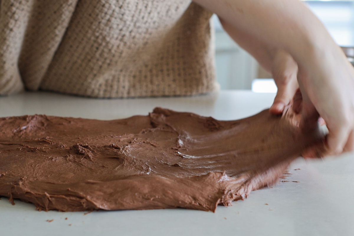 Hands stretching a chocolate dough into a rectangle.